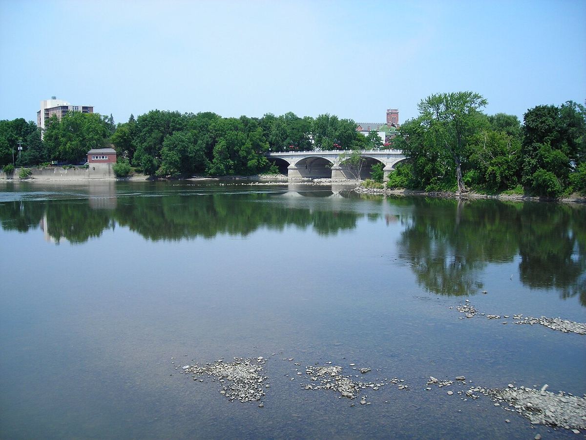 The Susquehanna River on a calm, sunny summer day in Binghamton, N.Y., lined with green trees and an arched stone bridge