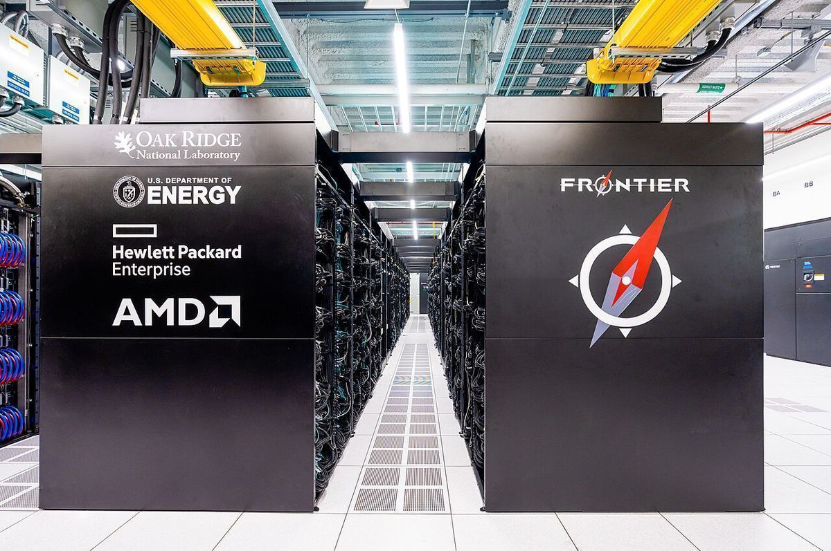 Rows of black supercomputer cabinets labeled Frontier, Hewlett Packard Enterprise and Oak Ridge National Laboratory in a bright data center