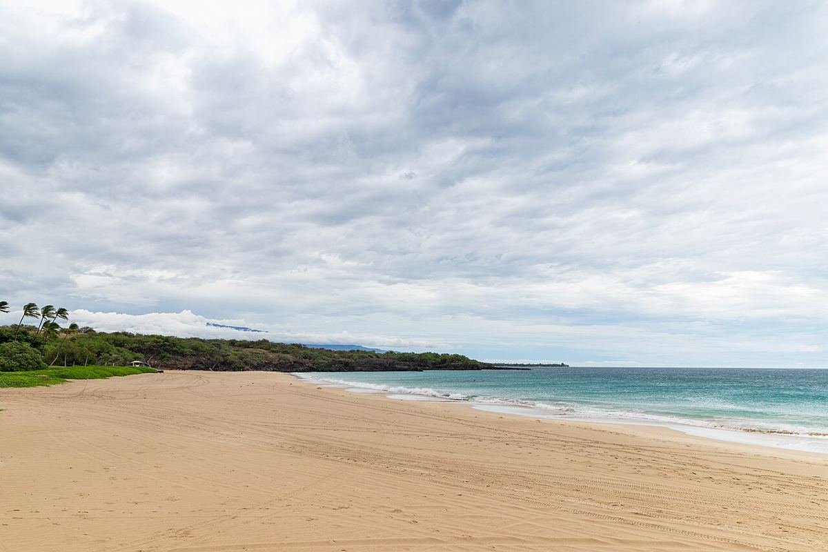 An empty sandy beach and turquoise surf under a cloudy sky at Hapuna Beach on Hawaii's Big Island