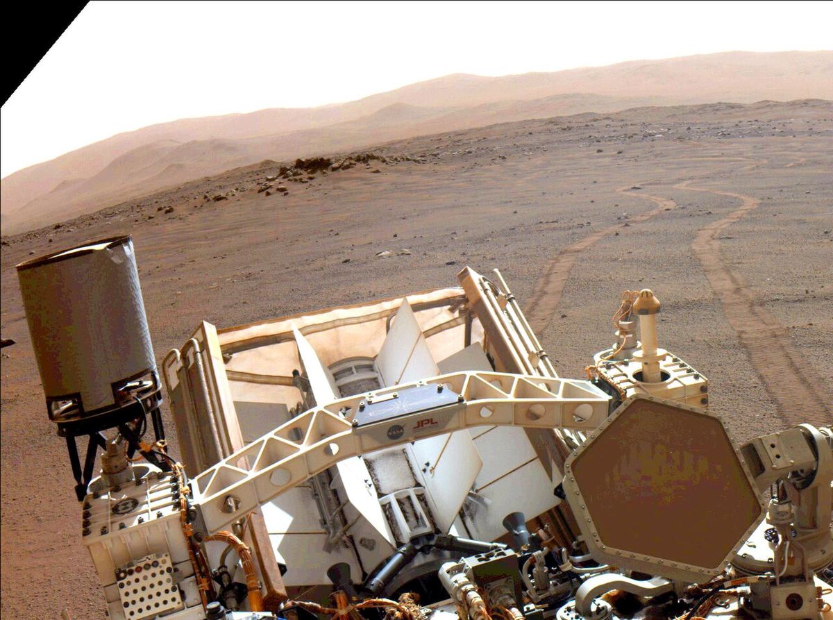 Wheel tracks curving across reddish Martian ground behind NASA's Perseverance rover, with hills on the horizon