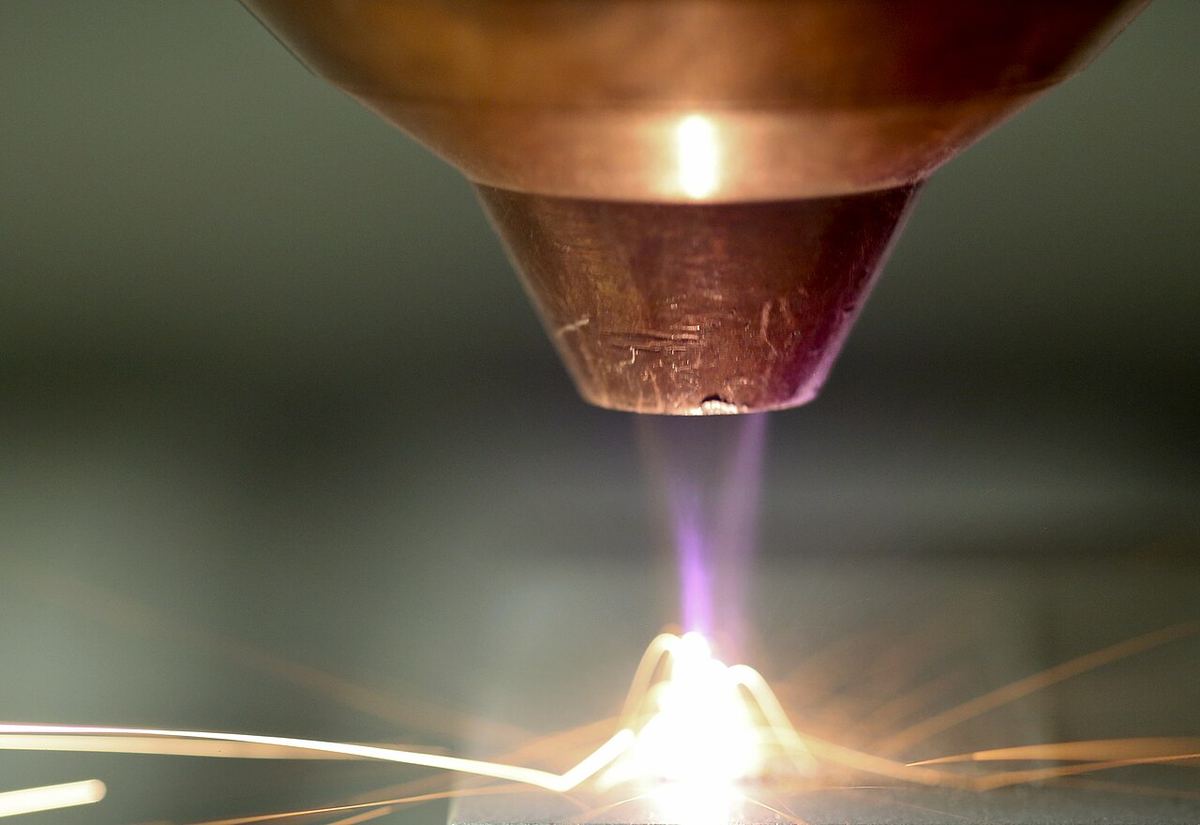 Close-up of a copper nozzle depositing glowing metal in a shower of sparks during advanced manufacturing