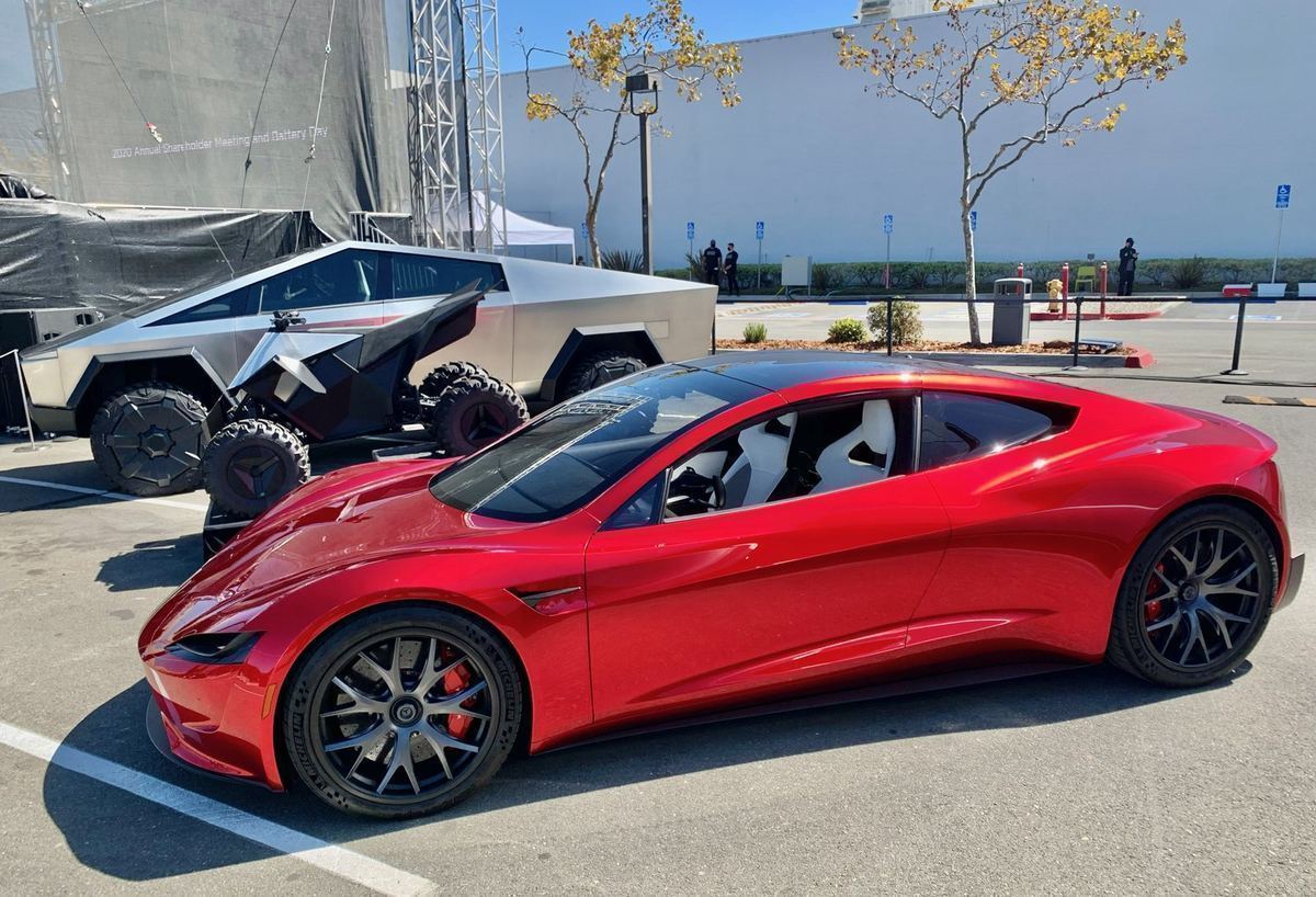 A red next-generation Tesla Roadster prototype parked outdoors, with a Cybertruck prototype behind it