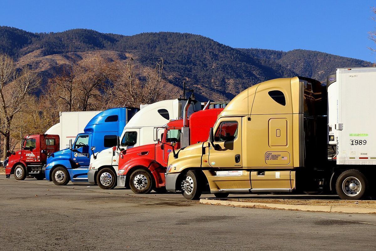 A row of colorful semi-truck cabs parked at a rest area below brown hills