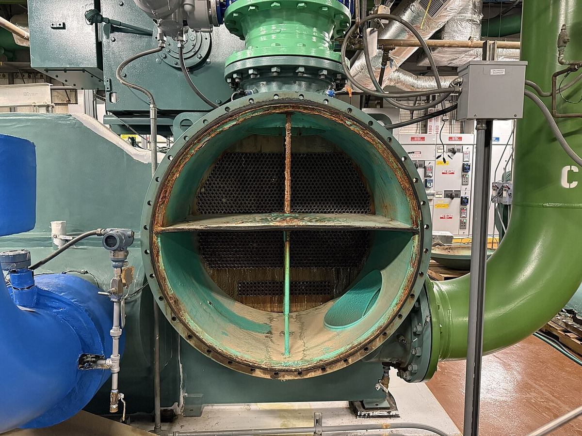 The opened heat exchanger of a large industrial chiller, with green and blue pipes in a mechanical room
